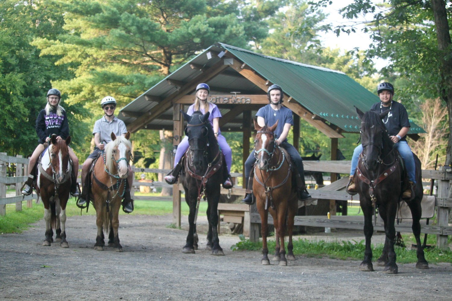 Five people on horses in front of a wooden shelter in a forested area.