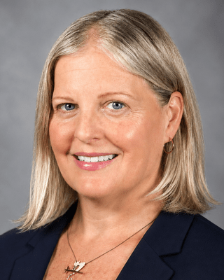 Smiling woman with shoulder-length blonde hair in a dark blazer.