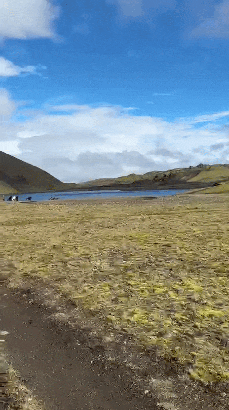 Scenic view of a lake with hills under a blue sky with clouds.